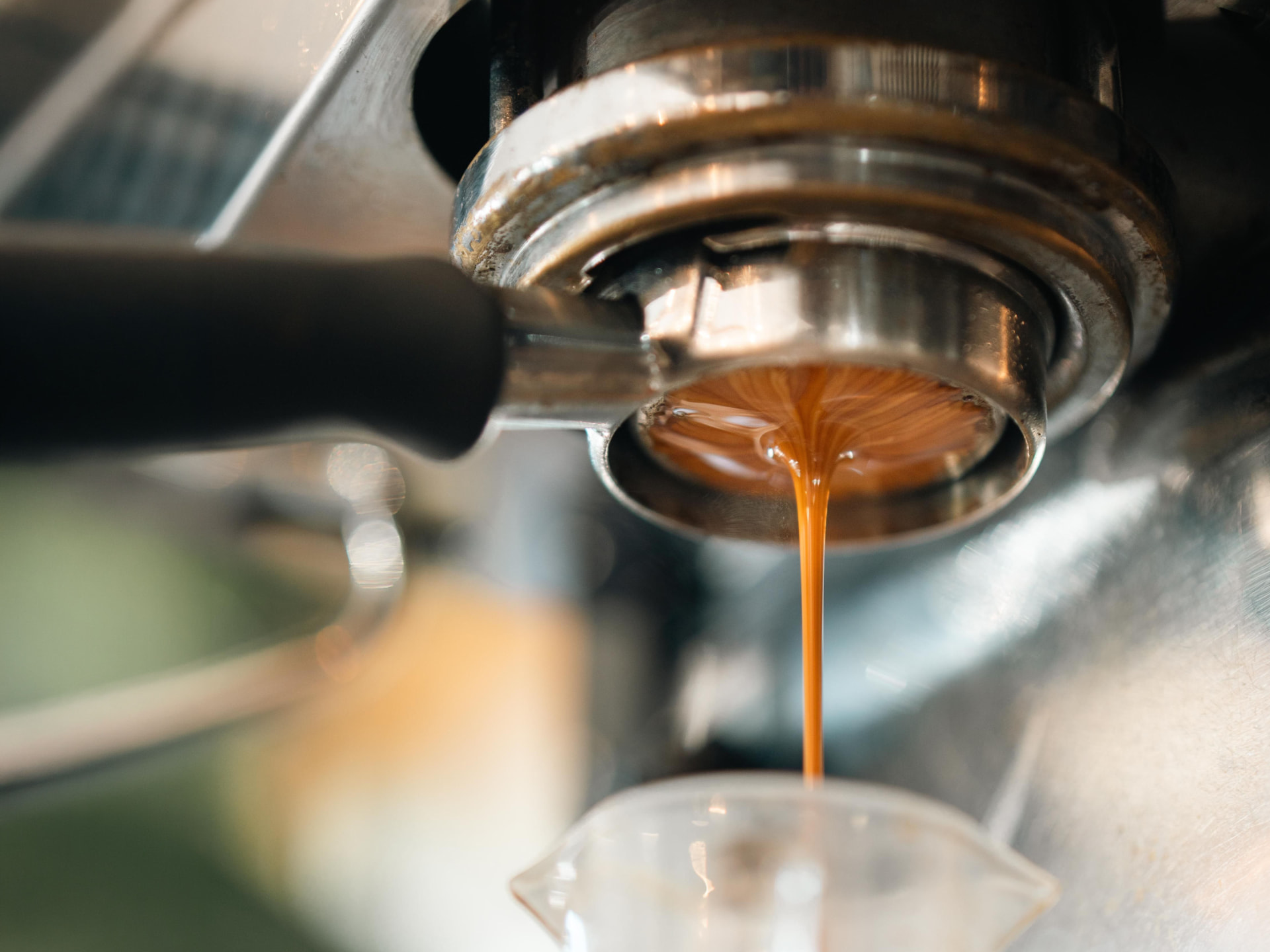 Espresso extracting from a bottomless portafilter into a clear glass pitcher on an espresso machine